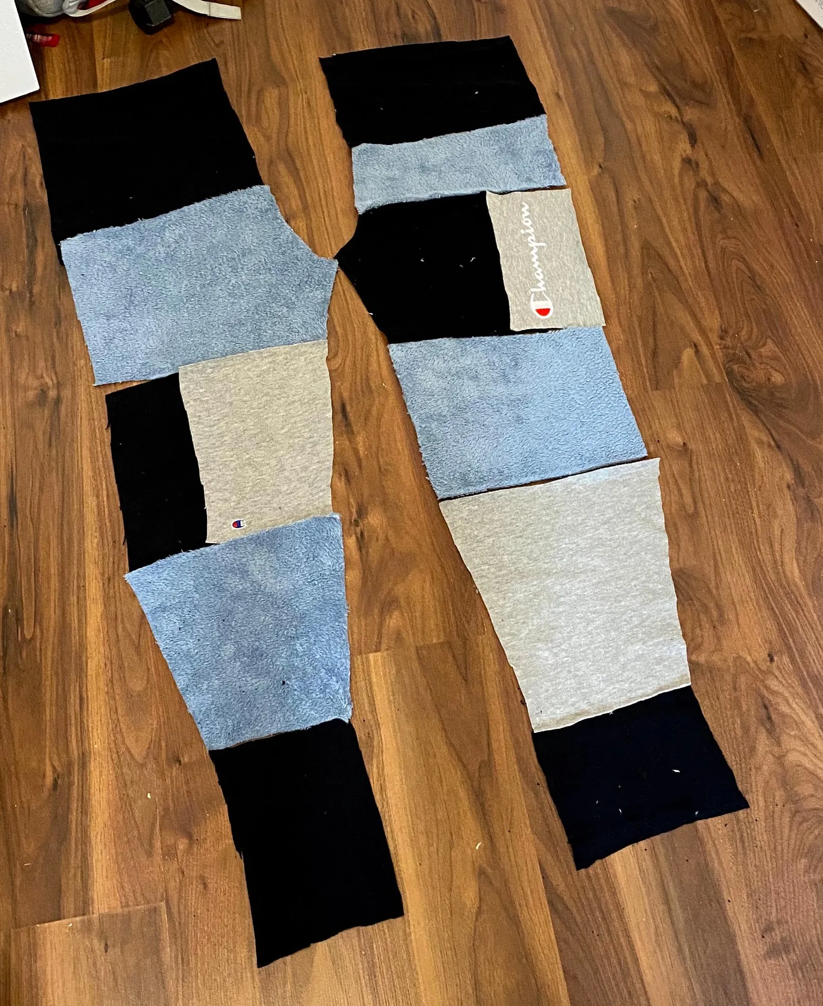 Cut panels of black, grey and blue sherpa fabric laid out on the floor in the shape of a pair of joggers