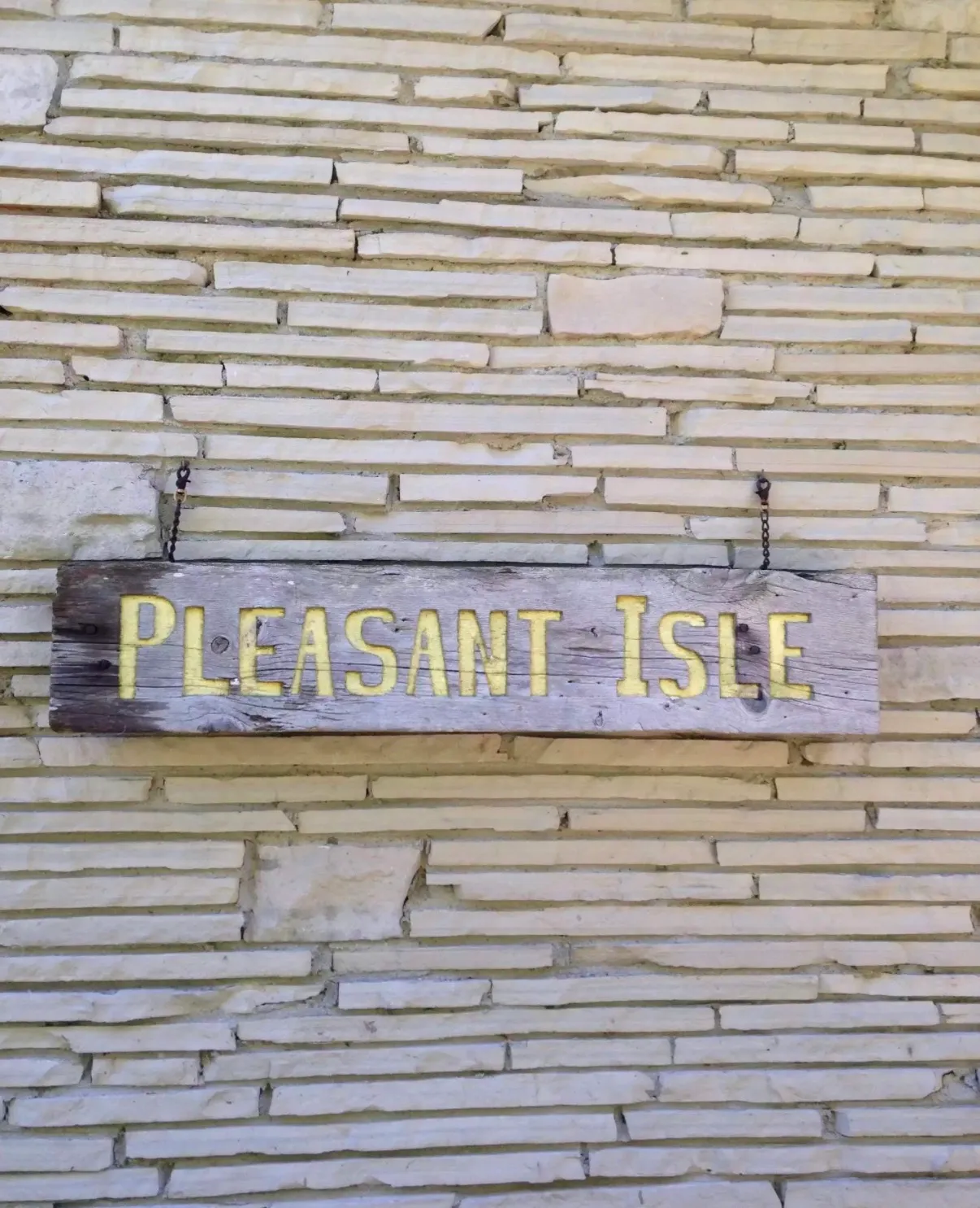 A weathered wooden sign reading Pleasant Isle, hanging on the cottage’s stone wall